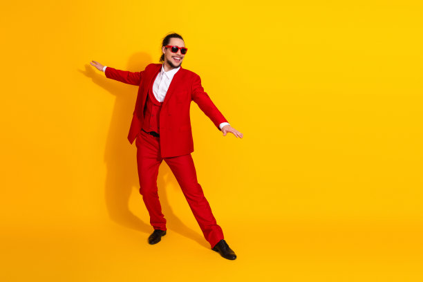 身穿醒目红西装的时尚男士，在明亮的黄色背景前，以奔放的热情舞动，是适合广告和推广的现代时尚生活方式素材。图片下载