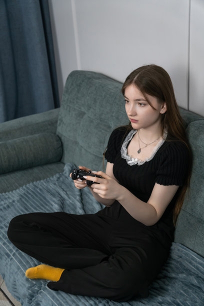 专心致志的年轻女孩坐在舒适的沙发上玩电子游戏，手握控制器，享受休闲时光。竖式照片图片下载