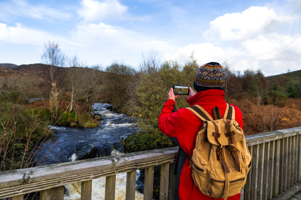 一位老人正用手机拍摄河流的照片图片下载