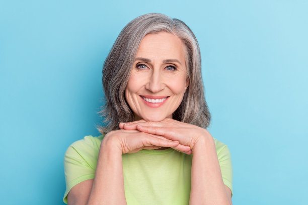 照片：一位快乐、积极、迷人的老年妇女在蓝色背景上露出灿烂的牙齿笑容图片下载