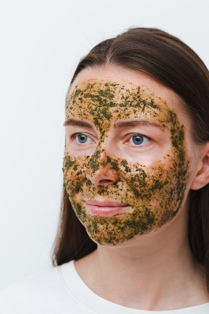 绿色天然自制面膜敷在脸上，一名年轻女孩或女人的肖像，白色背景。居家或沙龙的自我护理概念。竖直照片图片下载