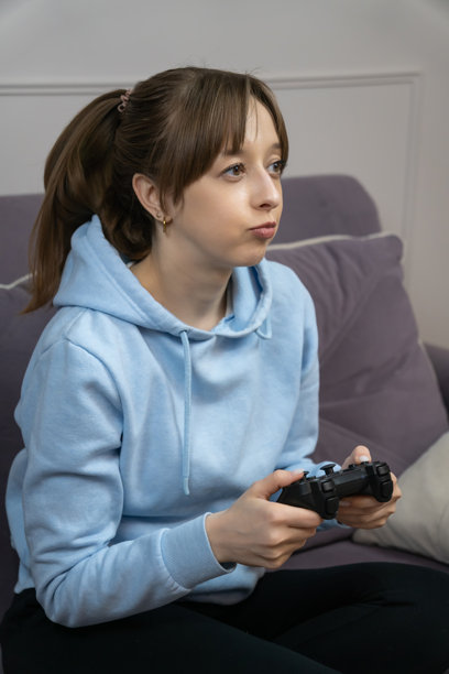 年轻女子在家里的沙发上享受休闲时光，手持游戏手柄，俏皮地噘嘴玩电子游戏。竖幅照片图片下载