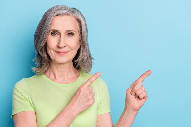 照片肖像：一位年长女性面带微笑，指向空白区域，背景为孤立的粉蓝色调。图片下载