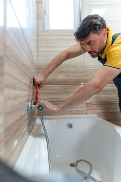水管工在白天时分，在现代浴室里修理浴缸水龙头图片下载