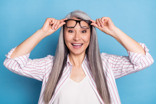 照片：一位惊喜、兴奋、快乐的老妇人举着眼镜，面带好心情，背景为蓝色图片下载