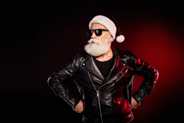 身穿黑色皮夹克和帽子的摇滚风圣诞老人，双手叉腰自信摆拍，背景为戏剧性的红灯，适合节日素材图图片下载