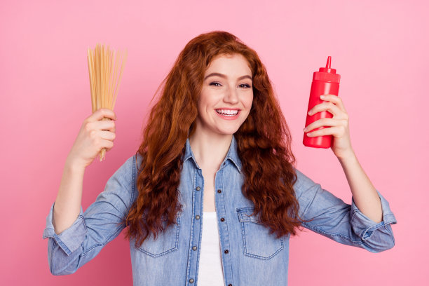 照片：可爱、快乐、漂亮的年轻女子，手拿意大利面，面带微笑，沾着番茄酱，孤立在粉色背景上图片下载