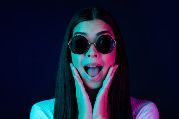 年轻千禧一代女士戴着眼镜，穿着白色毛衣，双手捂脸，在黑色深色背景下被孤立的照片图片下载