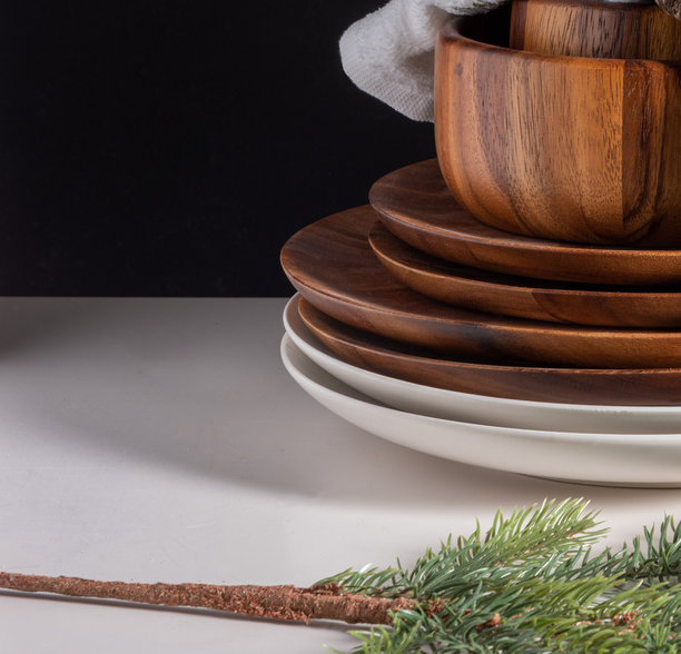 照片展示了深色乡村风木质餐盘和碗叠放在光滑的白色陶瓷餐具之上，并用一根低调的绿色人造松枝点缀。图片下载
