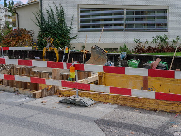 城市街道建筑工地，有红白安全护栏，挖掘机正在道路维修区作业。高质量照片图片下载