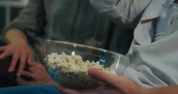 白人母亲和儿子晚上在家里的客厅沙发上一起放松，边看电视边吃爆米花。家庭生活方式概念。图片下载