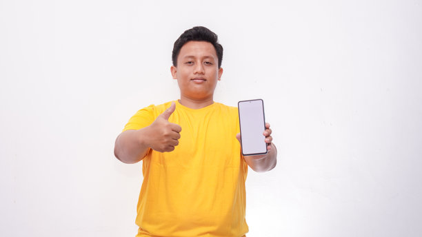 一名亚洲男子手持智能手机，屏幕朝向镜头，指向您，一位快乐的千禧一代男性正在推荐新的应用程序或移动网站，样机横幅拼贴。图片下载