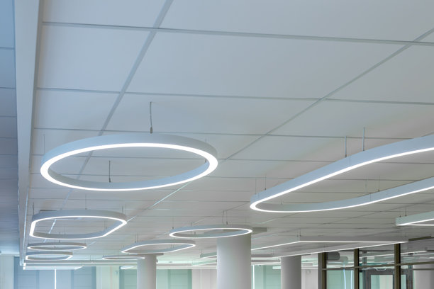 现代办公室天花板，配有圆形LED灯和白色网格面板。空置商业建筑内的悬挂式环形灯具。极简设计，适用于开放式办公室或大堂区域。实拍照片图片下载