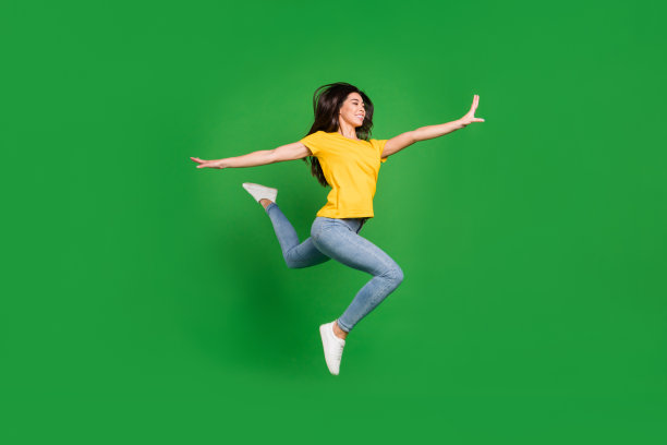 快乐活泼的年轻女子伸展身体，在绿色背景前开心地跳跃，全景照片图片下载