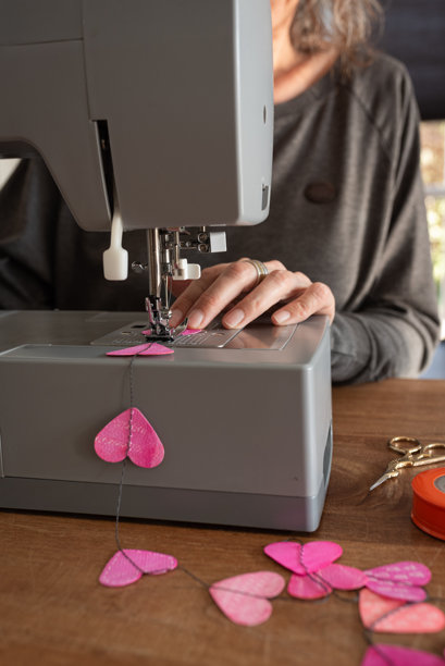 女子用缝纫机将手绘的纸心缝制成花环图片下载