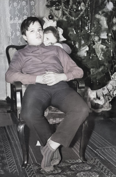 一名女孩抱着她的弟弟，复古风格的肖像，摄于1973年，背景是新年树。图片下载