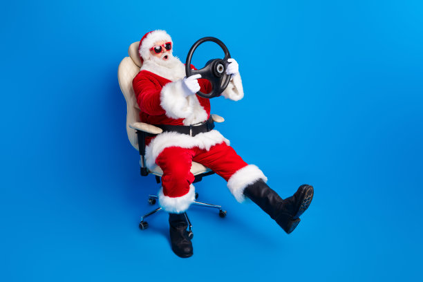 穿着时尚圣诞老人服装外套的退休老人，全身照，坐在扶手椅驾驶位上，手持舵，在蓝色背景上图片下载