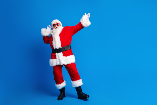 退休老人身穿时尚圣诞老人服装外套，在蓝色背景前全身跳迪斯科舞的照片图片下载