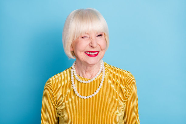 照片：时髦可爱的短发老太太眨眼，身穿衬衫项链，孤立在蓝色背景上图片下载