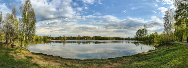 湖岸、树木、水面倒影、鸭子以及阴沉的雷雨云天空，阳光透过云层照耀。春季。俄罗斯。下诺夫哥罗德。斯维特洛亚尔斯科耶湖。2025年4月。照片。图片下载