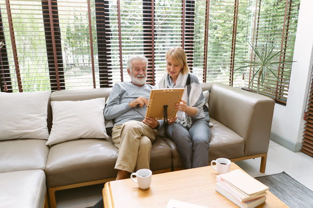 客厅里，一对年迈的夫妇坐在沙发上，看着相框里家人的照片。退休老年夫妇生活方式概念。图片下载