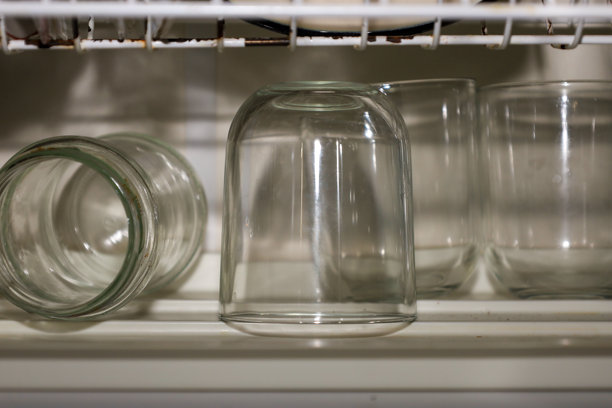 干净的玻璃器皿在架子上晾干：一个倒置的饮水杯和几个透明的罐子。这张特写照片描绘了洗涤后的家庭场景，突出了玻璃的光泽和洁净。图片下载