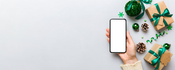 带有文字空间的圣诞节样机。圣诞广告，应用程序模板。手持带有空白屏幕的手机，背景为桌面。新年快乐和圣诞节俯视拍摄。图片下载