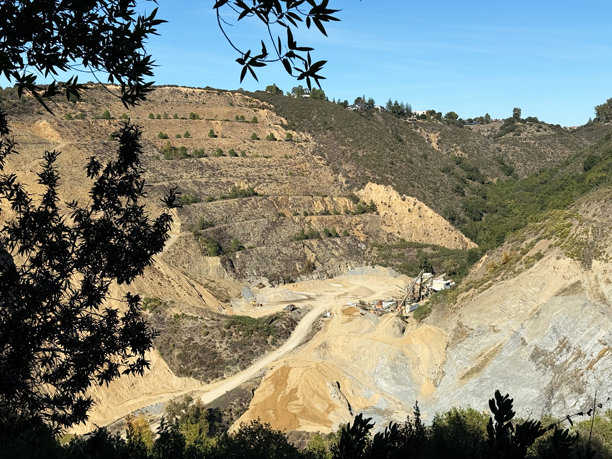 山地丘陵中的露天采石场景观，周围环绕着干枯的植被和稀疏的树木，拥有梯田状的斜坡、建筑机械和工业建筑。图片下载