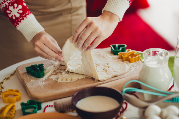 圣诞节期间，在舒适的居家厨房台面上，一双巧手正在制作圣诞饼干，旁边放着面团、饼干模具和牛奶，充满了欢乐的节日烘焙氛围。图片下载