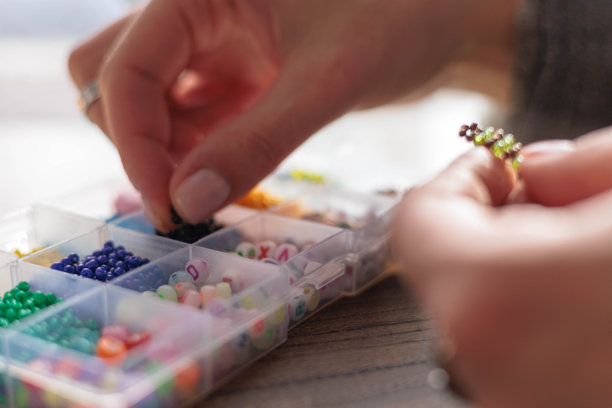 制作手工饰品。桌上的珠子盒子。俯视视角，可见女性双手图片下载