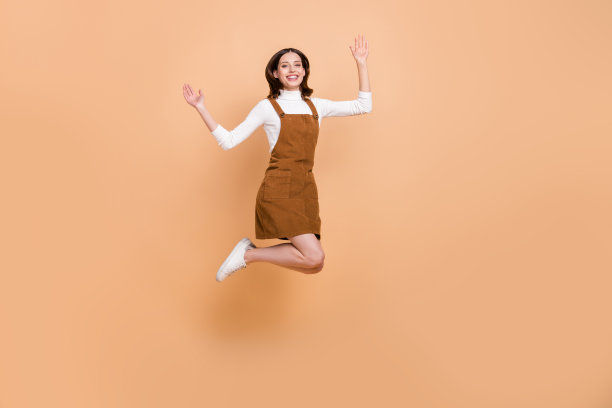 一个漂亮、满意、开心的女士的全身照，她举起双手，在米色背景前玩得很开心，照片是全景的。图片下载