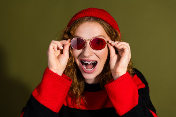 戴着红色绒球帽、圆形太阳镜和条纹毛衣的年轻女孩，面带微笑，用于时尚生活方式图库照片图片下载