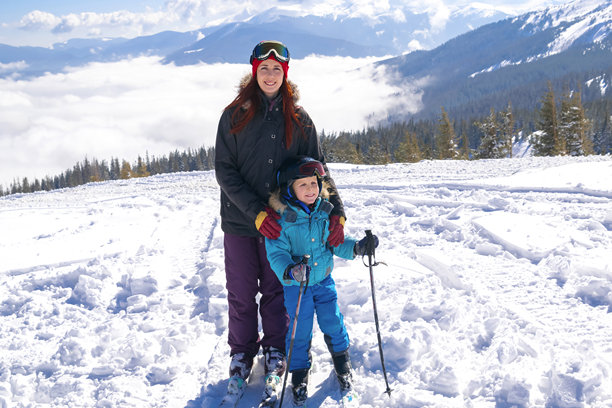 年轻的运动女性在山地高山滑雪度假村与儿子一起滑雪玩乐。母子家庭享受极限运动休闲活动。图片下载
