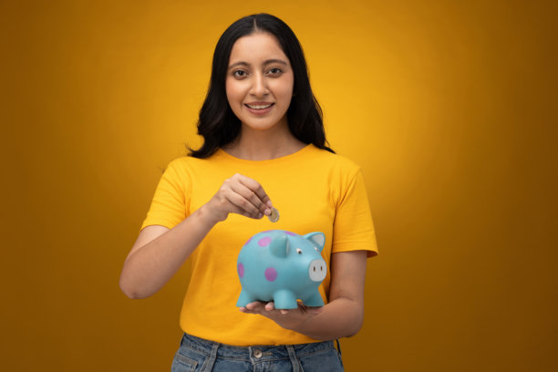 身穿黄色T恤的年轻漂亮女孩手持存钱罐，在黄色背景下拍摄的肖像照片图片下载