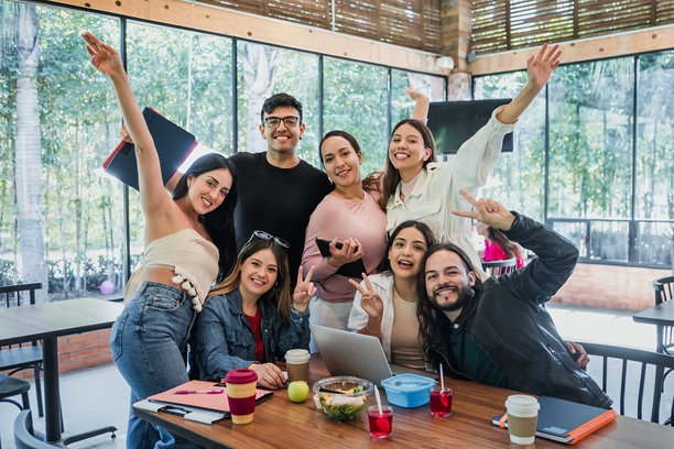 墨西哥拉丁美洲大学城，一群拉丁裔大学生在早餐时分聚集在食堂里，一边使用笔记本电脑和笔记本，一边学习，拍下这张自拍肖像照。照片中的是年轻的西班牙裔男女。图片下载
