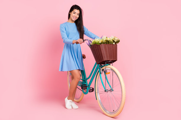 年轻女孩全身侧面照片，面带快乐积极的微笑，车篮里装着鲜花，在柔和的彩色背景下独立展示图片下载