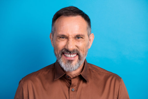 自信的成熟商人，身穿棕色衬衫，在蓝色背景前微笑，用于企业商业生活方式图库照片图片下载