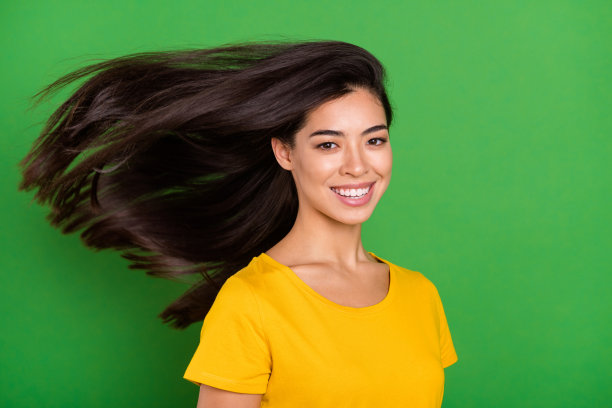 一位长着棕色长发的女孩在风中飘扬，喜悦地笑着，背景是明亮的绿色，留有复制空间的照片肖像图片下载