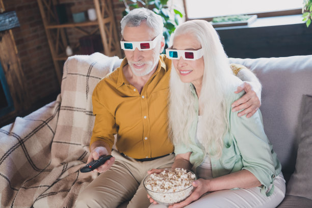 迷人的老年夫妇坐在沙发上，拥抱在一起，在阁楼工业风格的室内家居中看电视，玩得很开心。图片下载