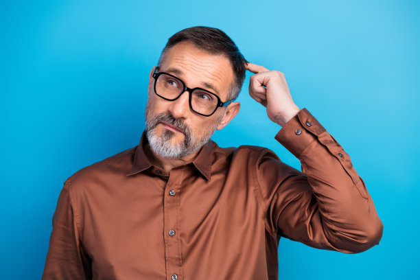 穿着棕色衬衫、戴着眼镜的自信成熟的商人在蓝色背景前思考，用作图库照片图片下载