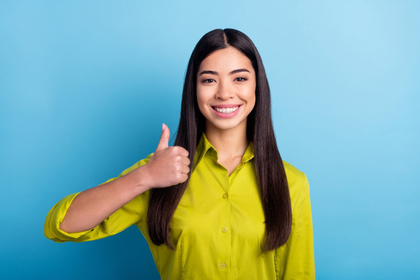 年轻女孩开心积极的微笑竖起大拇指，喜欢酷炫的广告建议选择，在蓝色背景上很棒，孤立图片下载