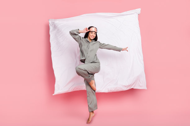 身穿可爱睡衣的迷人女士，戴着眼罩，笑容满面地在粉色背景前高高跃起，全长照片图片下载