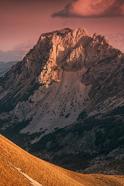 山地景观，有岩石嶙峋的山峰和斜坡，温暖的阳光在金色时刻的天空下营造出戏剧性的对比图片下载