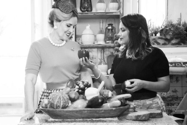 一位20世纪50年代的家庭主妇和她的女儿在厨房里分享着默契和温柔的时刻。这张黑白照片突显了日常场景的宁静和深情。图片下载