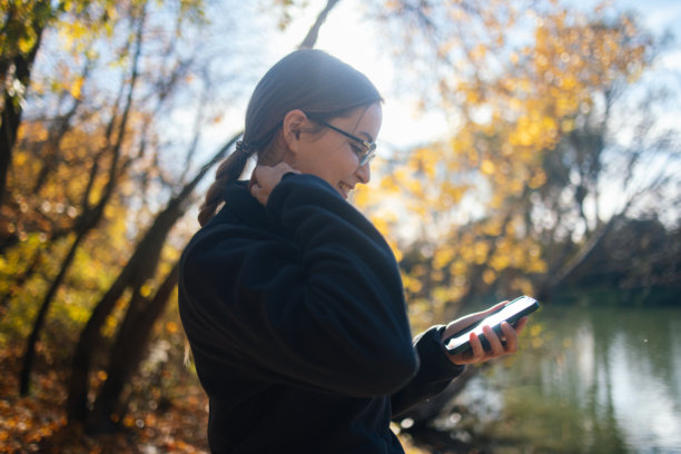 秋季，女子在河边查看手机的素材照片图片下载