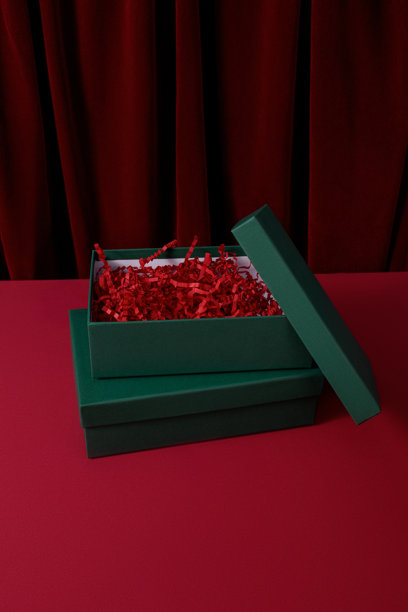新年和圣诞节主题图片，明信片样机，打开的绿色礼品盒，内有红色纸屑，背景为红色天鹅绒窗帘，礼品包装图片下载