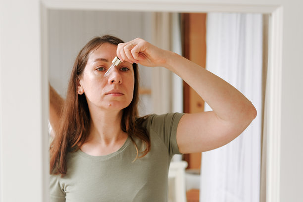 一位四十多岁的女性在早晨进行面部自我护理，她正从玻璃滴管中取用精华液涂抹于面部皮肤。护肤品。女性用油性滴管涂抹精油。化妆品广告。健康。健康。健康。健康。健康。健康。健康。健康。健康。健康。健康。健康。健康。图片下载