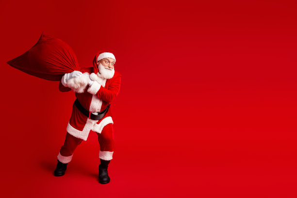 圣诞老人背着大红袋子在明亮的影棚里摆姿势，为圣诞季准备，充满节日魔力，可用于素材图片下载