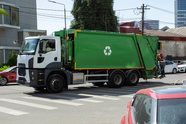 格鲁吉亚巴统 - 2025年4月1日：白天，城市区域内一辆绿色回收卡车和工作人员正在收集废弃物的照片图片下载
