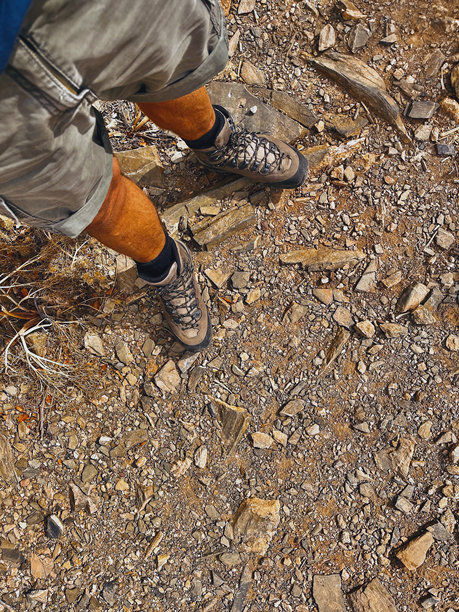 灰色短裤和灰色登山靴的男性腿部，在崎岖的山路上。俯视角度。图片下载